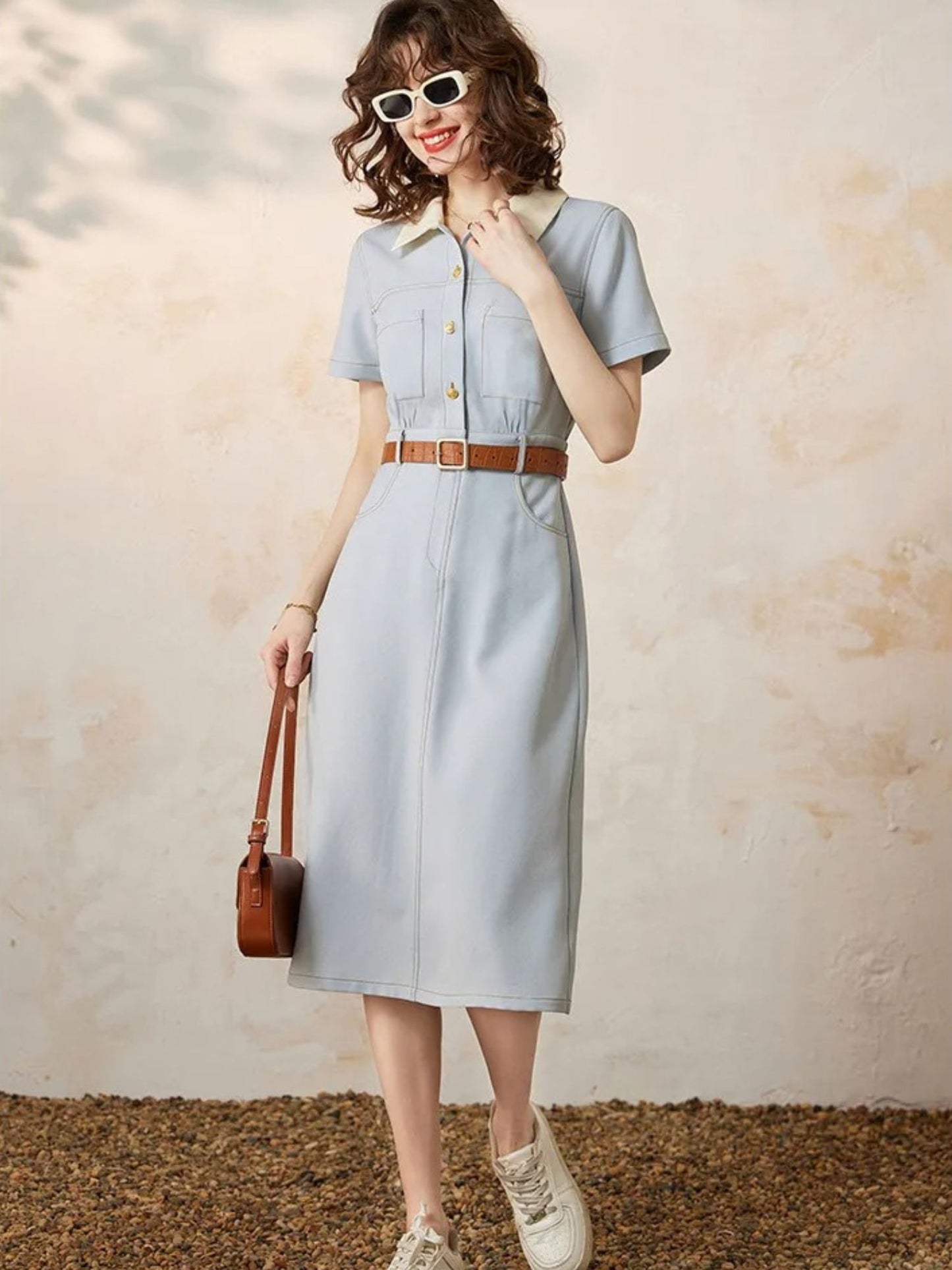 Woman posing in light blue collared dress with belt, holding bag
