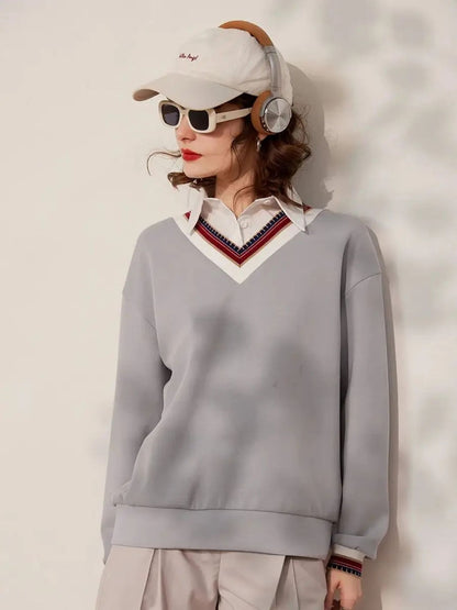 Front view of woman wearing grey V-neck sweatshirt with striped neckline