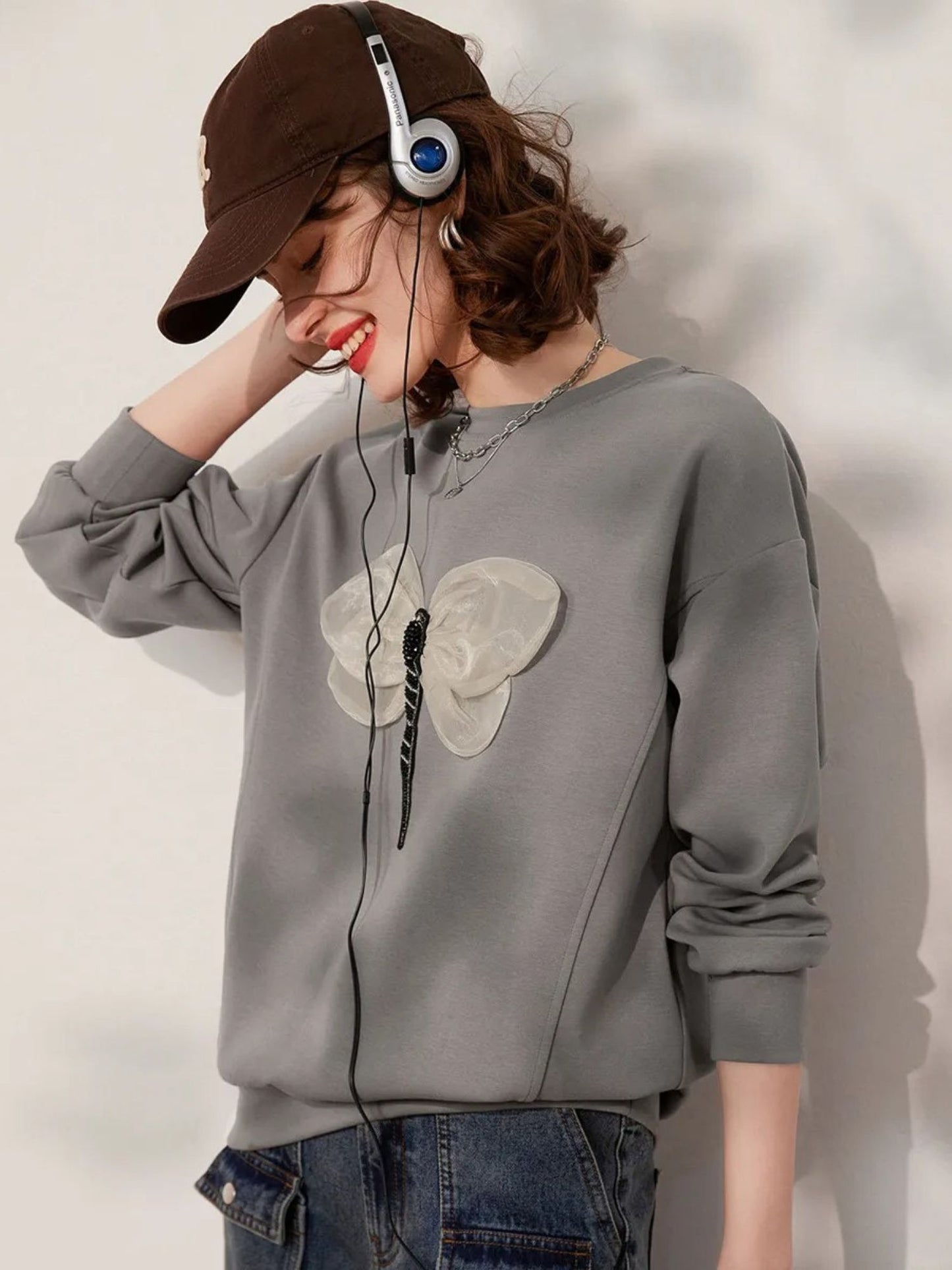 Side view of grey embroidered sweatshirt with jeans and cap