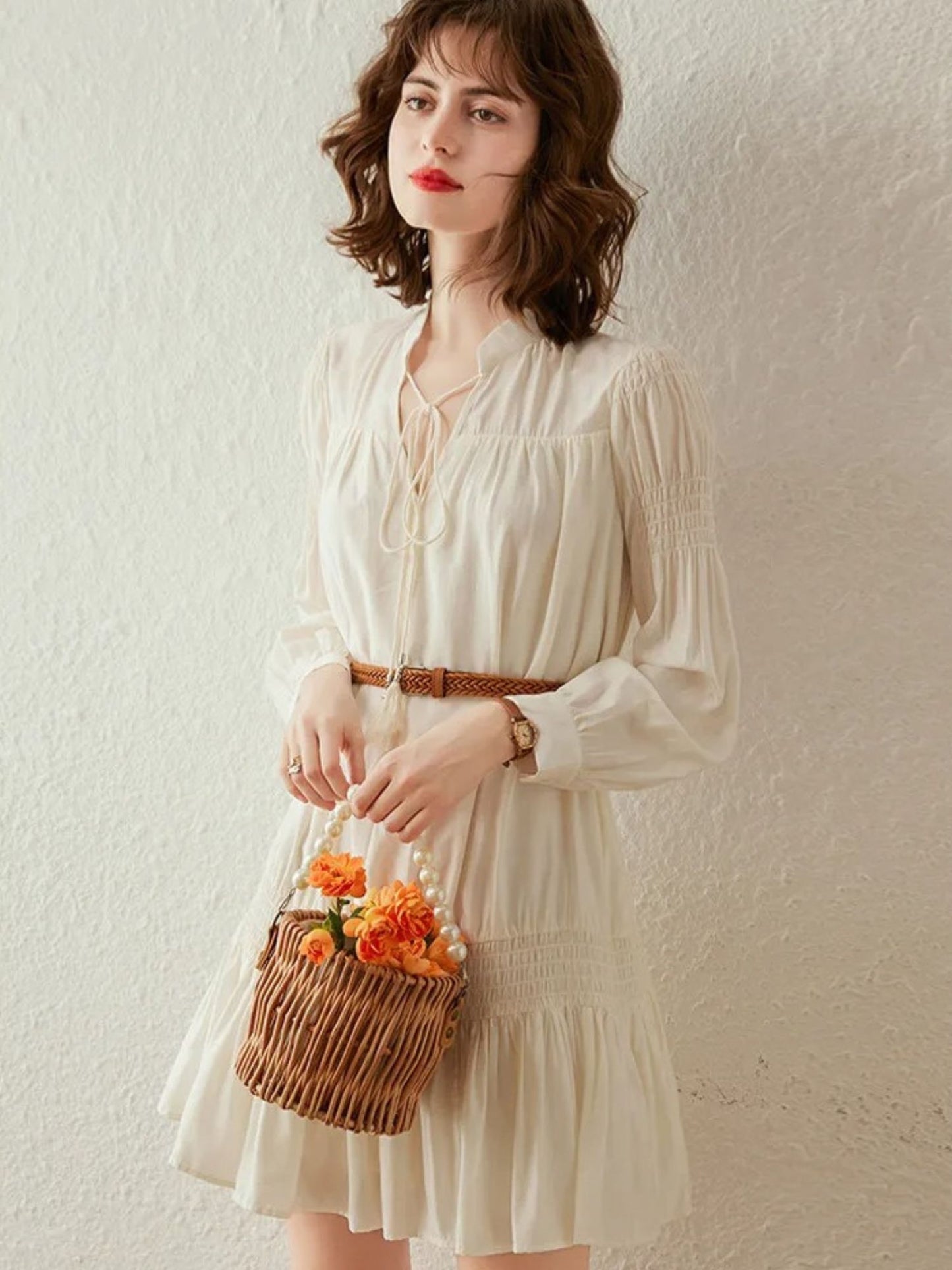 Woman standing in cream pleated mini dress with long sleeves