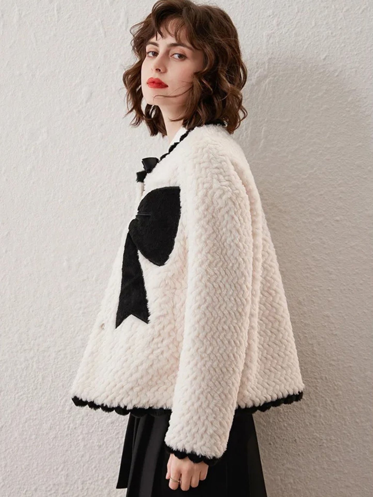 Side view of woman in white cardigan with black bows, posing with one hand in pocket