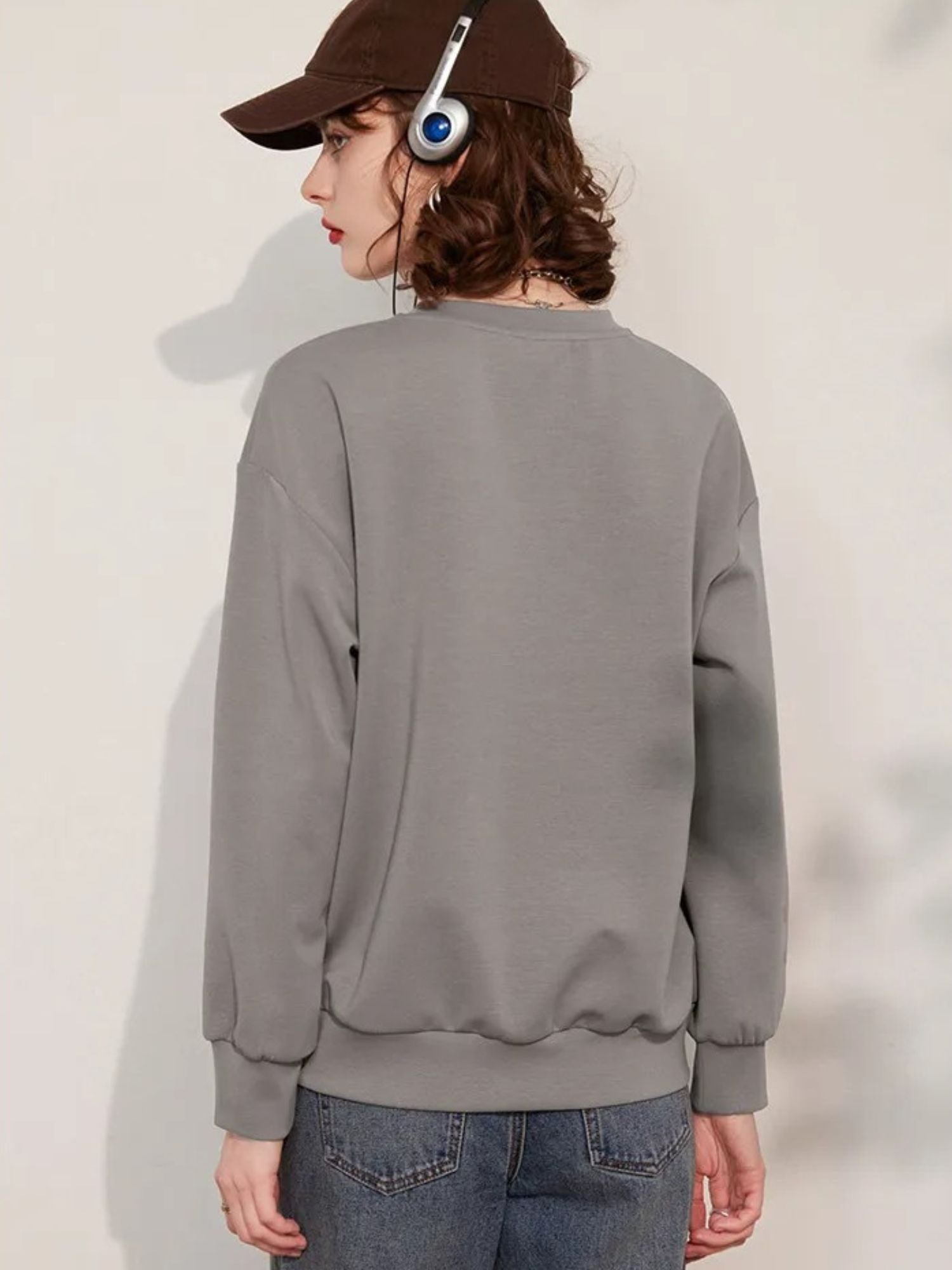 Back view of a woman wearing a grey jumper with a 3D dragonfly decoration on the front, paired with denim shorts