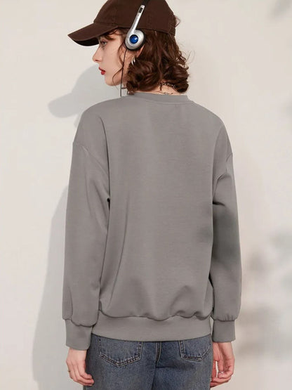 Back view of a woman wearing a grey jumper with a 3D dragonfly decoration on the front, paired with denim shorts