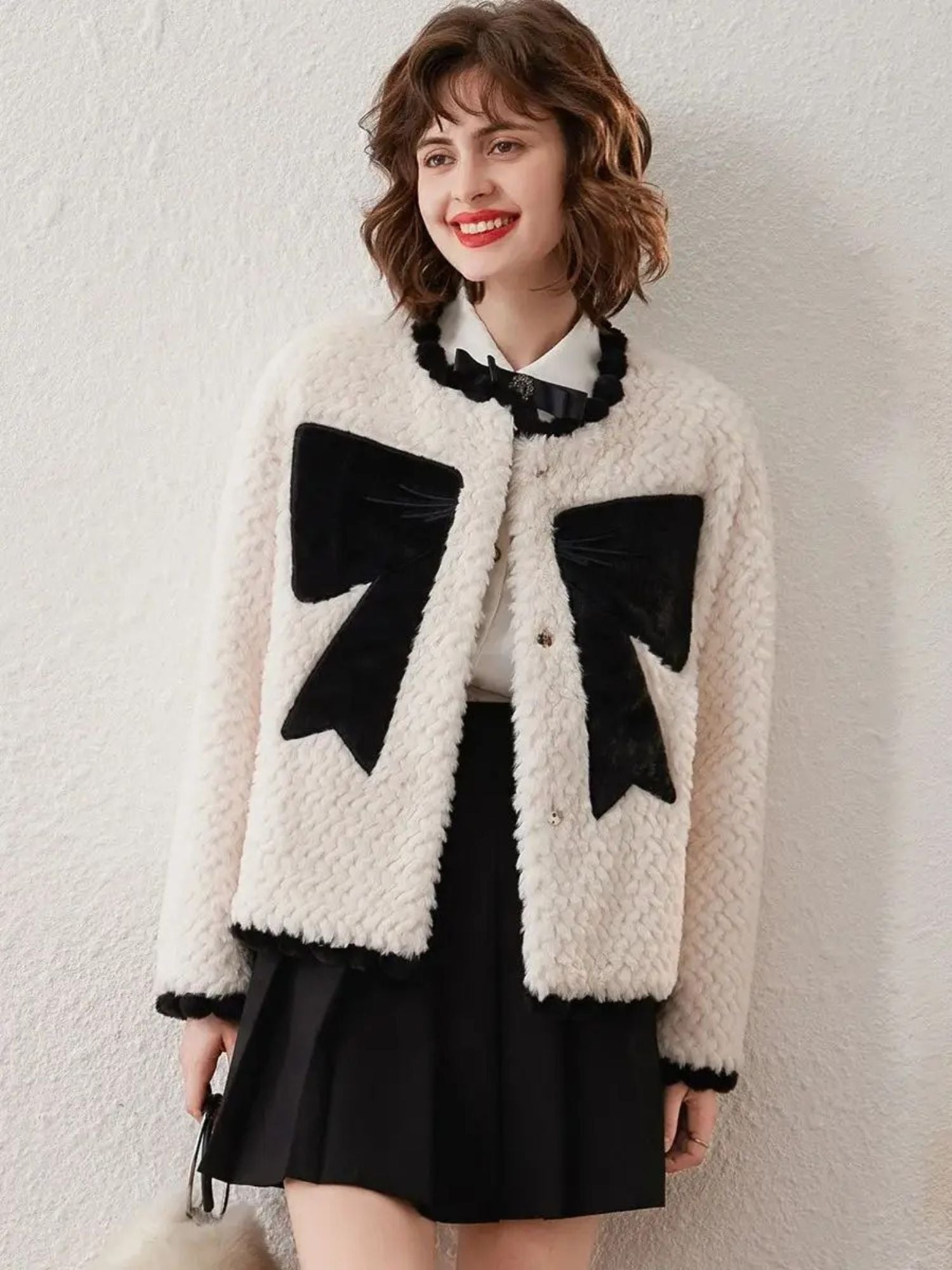 Woman in white cardigan with black bows, smiling and facing forward