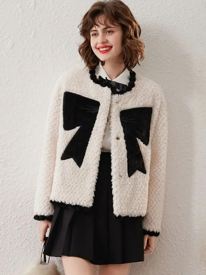 Woman in white cardigan with black bows, smiling and facing forward