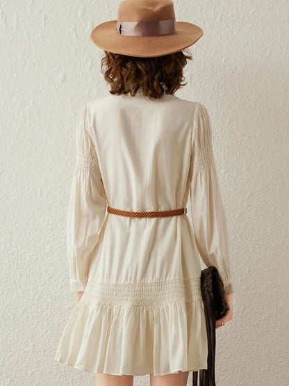 Back view of a woman wearing a cream boho-style long sleeve dress with a tie detail in the neckline and a brown belt