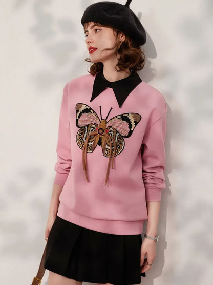 Woman wearing a pink sweatshirt with large butterfly embroidery, styled with a black skirt and beret