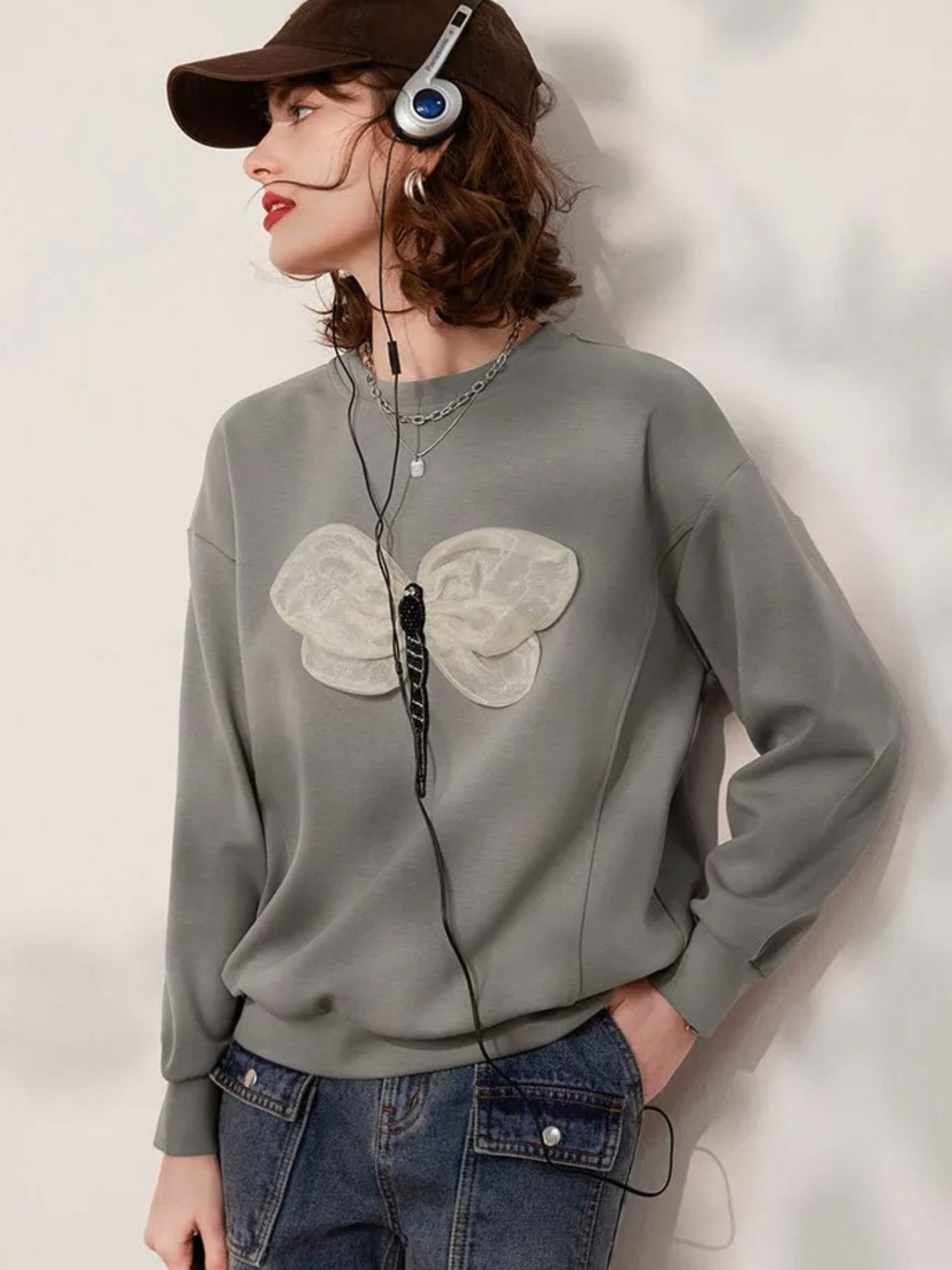 Angled view of grey sweatshirt with butterfly embroidery, styled casually with jeans