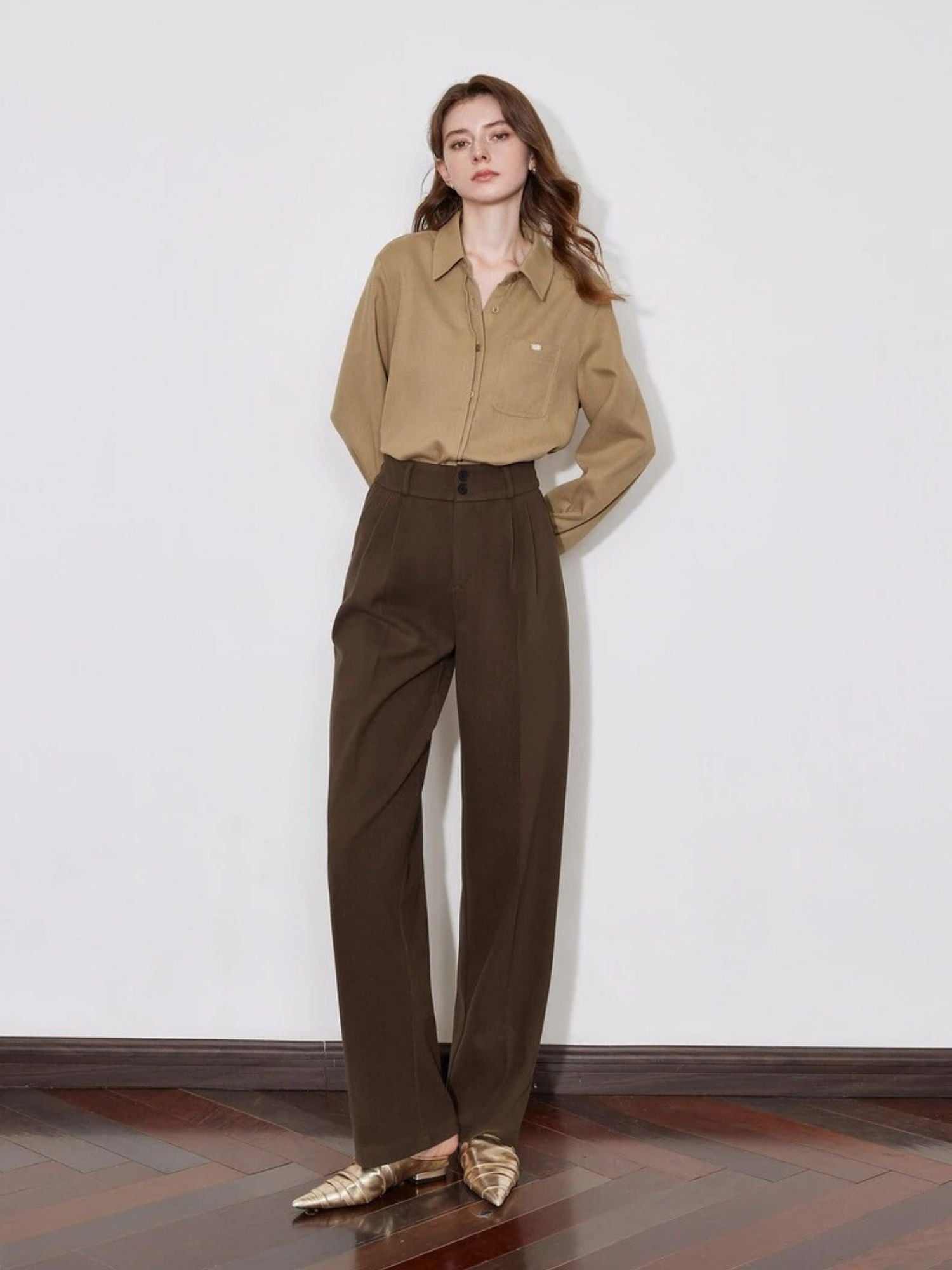 A model wearing a brown button up shirt paired with some dark brown high-waisted pleated pants