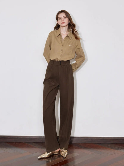 A model wearing a brown button up shirt paired with some dark brown high-waisted pleated pants