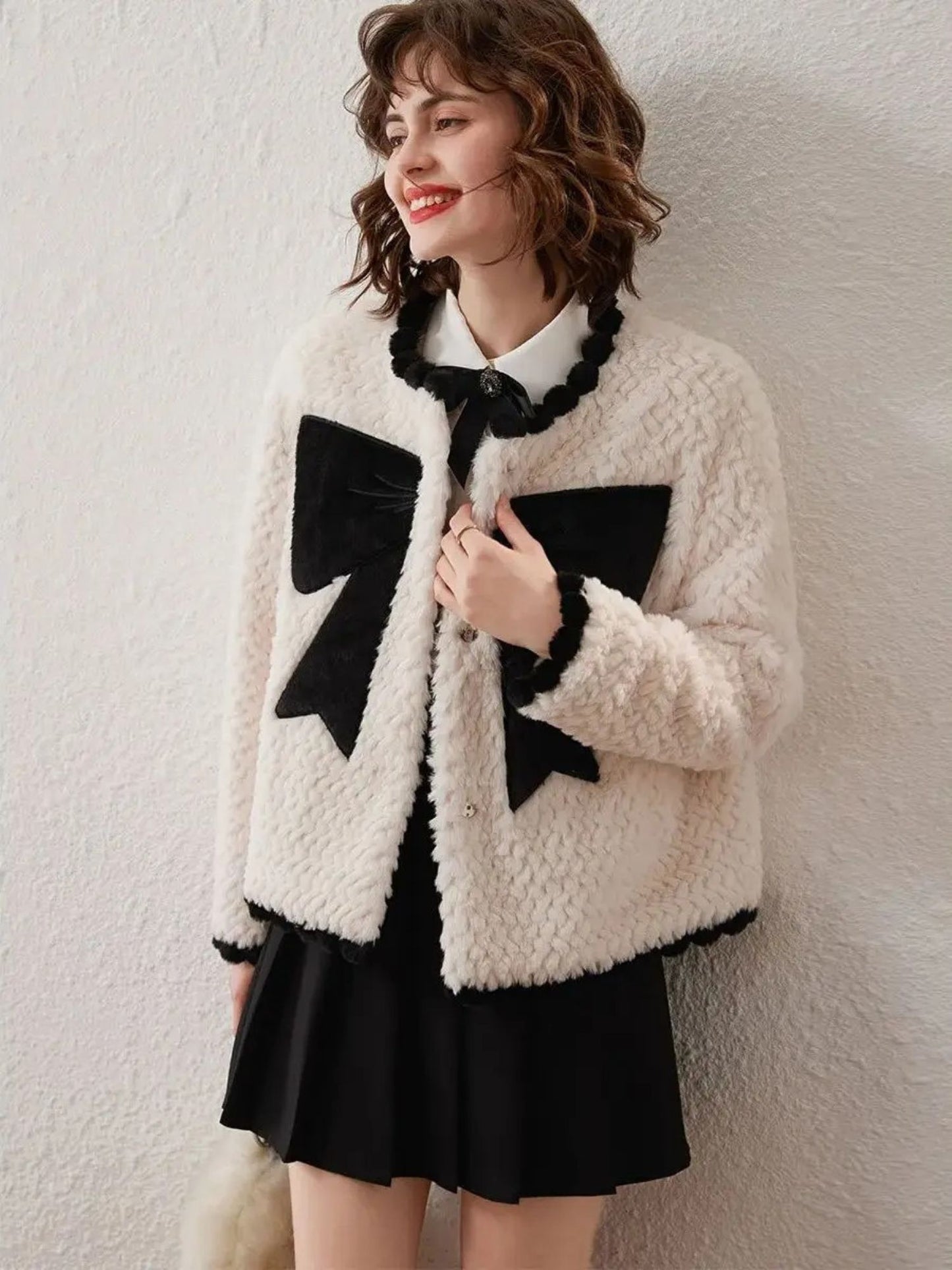 Woman in white cardigan with black bows, standing sideways and looking back