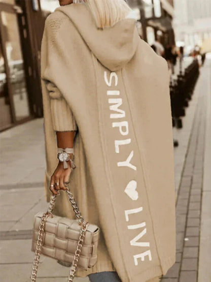 Person wearing a beige hoodie with 'Simply Live' text, holding a matching handbag on a city street.